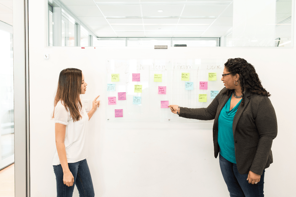 Two professionals mapping CRM requirements with sticky notes on a whiteboard